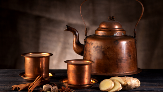 A kettle and two cups of chai, surrounded by spices (Cinnamon, cardamom, ginger)